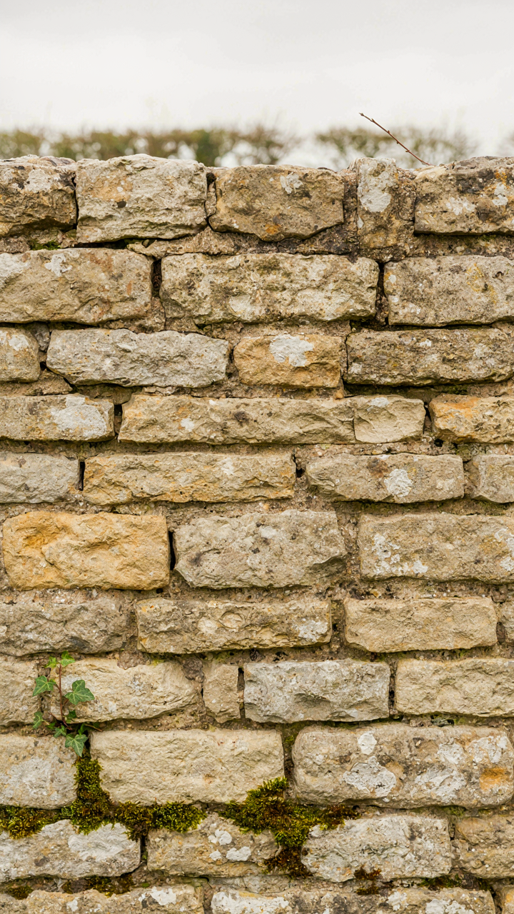 A weathered stone wall of a farmhouse, showing variations in color and texture.