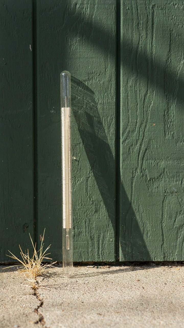 A thermometer next to a dark she shed exterior under the sun.
