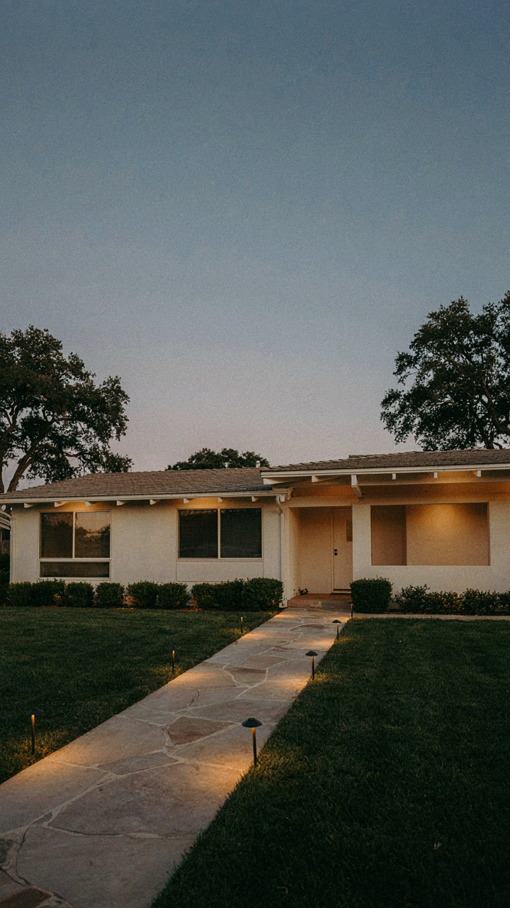 Path lights cast an upward glow on a mid century ranch house at dusk.
