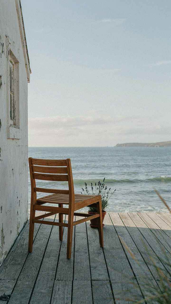 A single minimalist teak chair on a coastal cottage porch looking at the ocean.