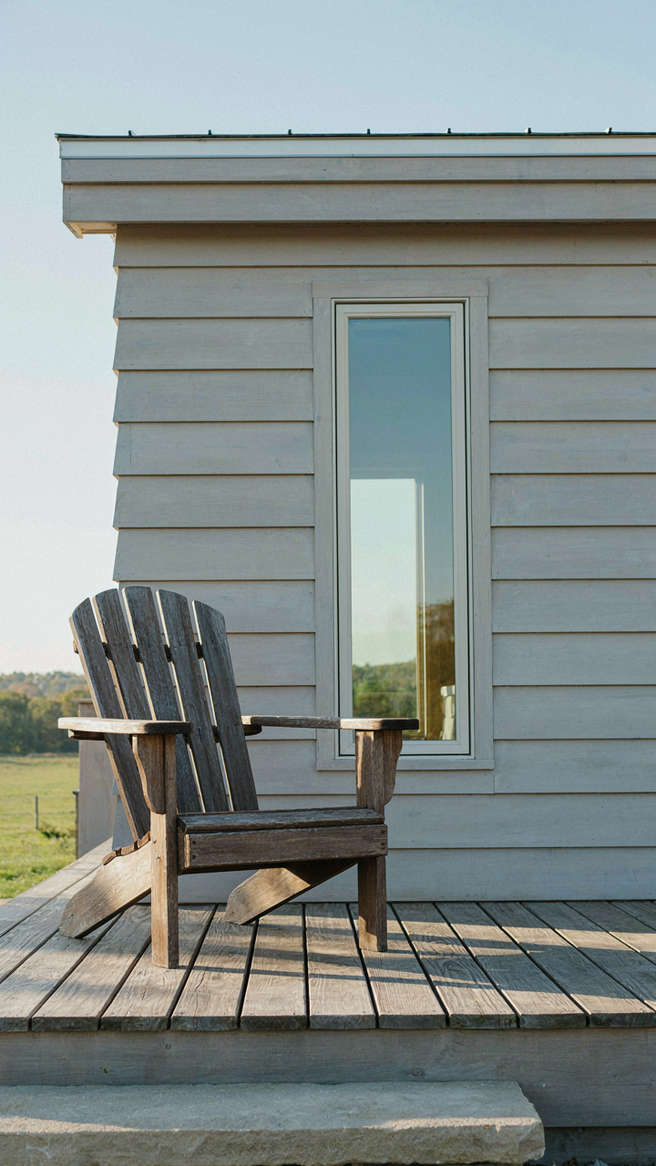 A single wooden Adirondack chair on a very clean tiny cabin porch.