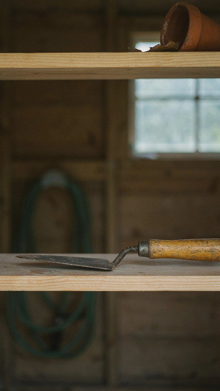 A gardening trowel with a date marked on its handle sits on a shed shelf.