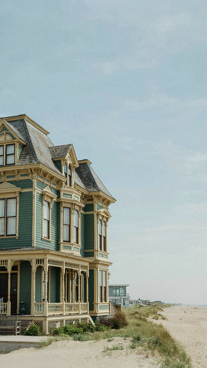 An ornate Victorian-era house with many dormers stands in a coastal setting.