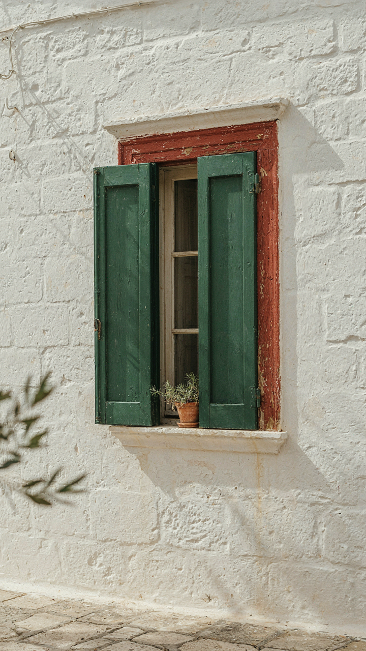 A whitewashed stone wall with a green shutter and red terracotta trim.