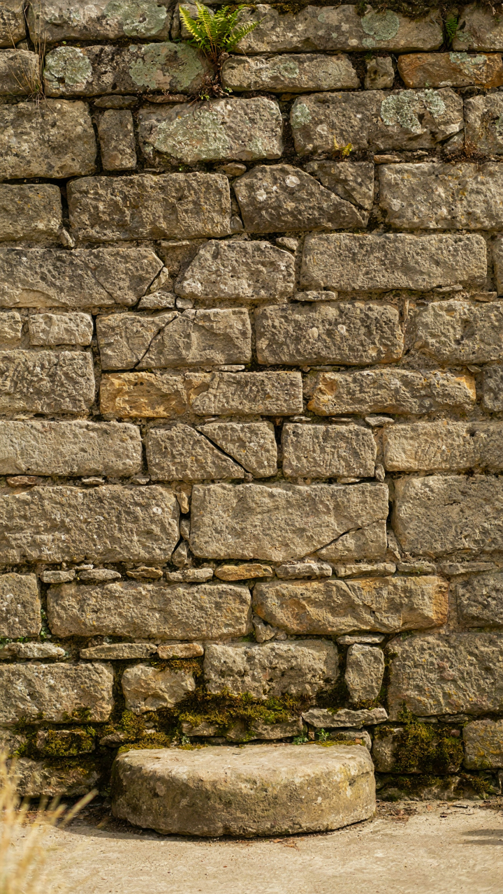 A close up of an ancient, unevenly weathered stone wall with moss.