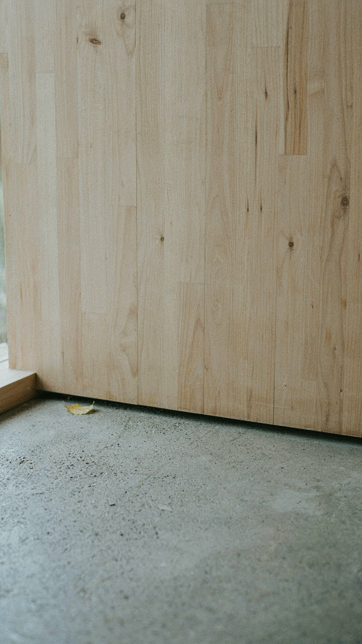 A close up view of a raw concrete floor against a simple birch wood wall.