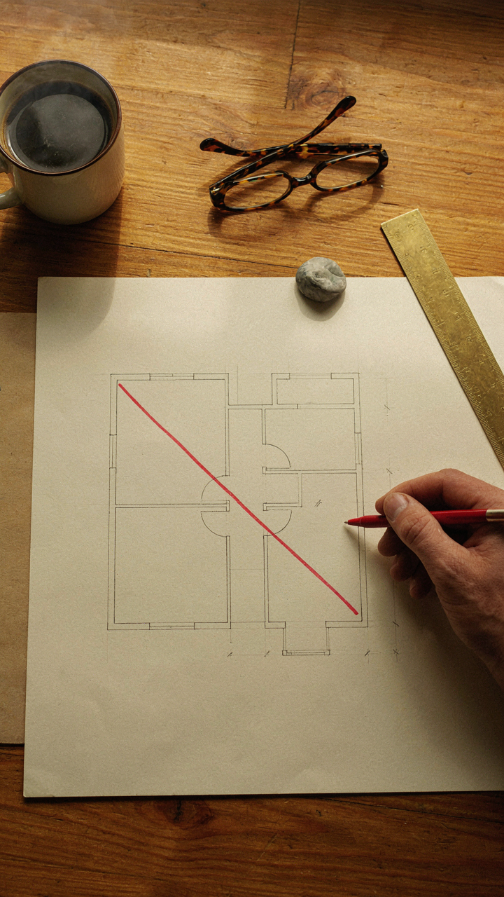 A hand with a red pen marking a basic floor plan sketch.