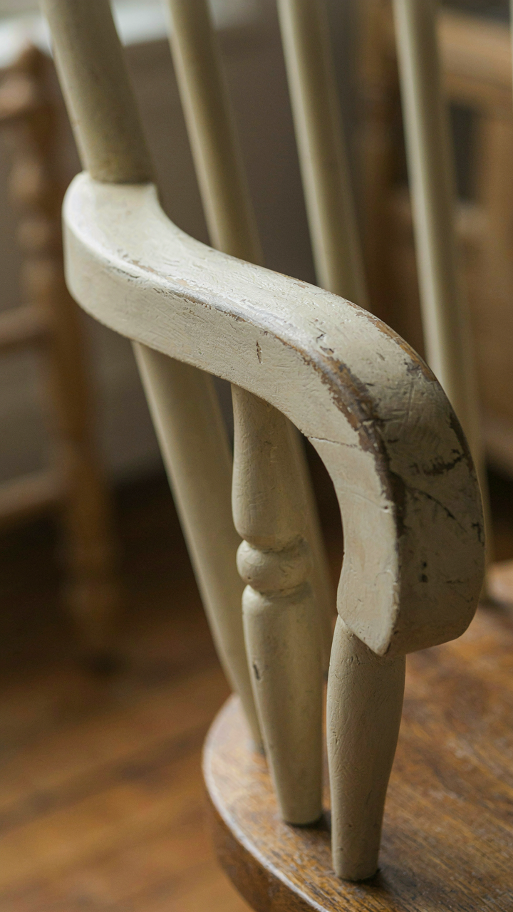 A close-up of a Windsor chair armrest with paint worn from use.