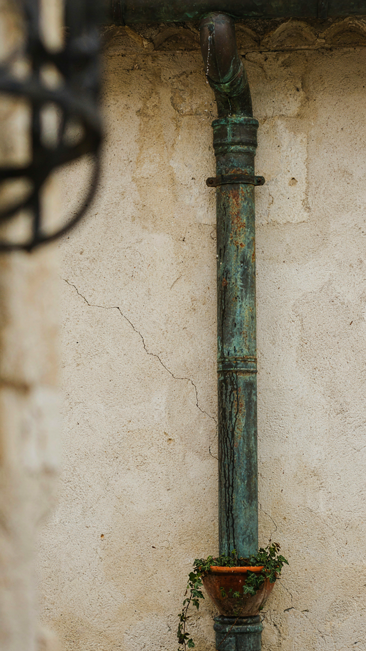 An oxidized copper downspout with green patina on a stucco French cottage.