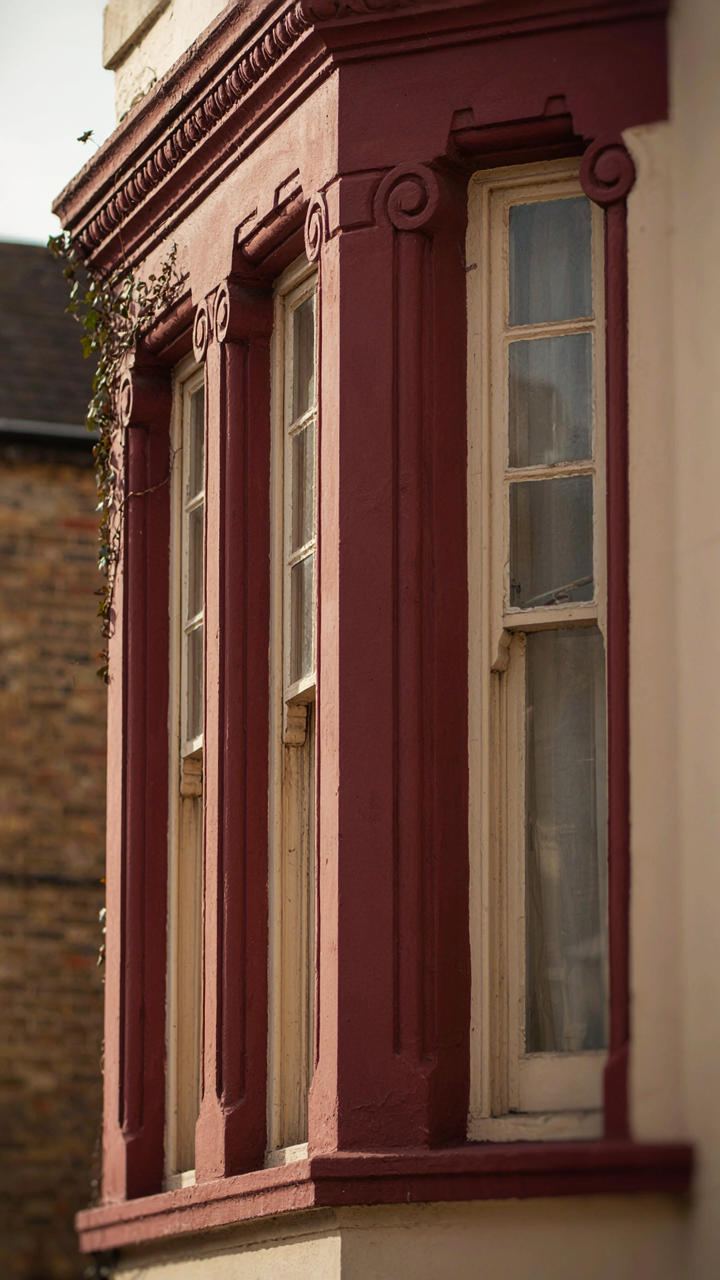 A bay window on a Victorian house with deep burgundy and cream trim.