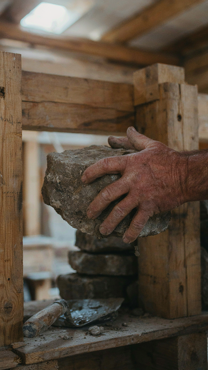 A stonemason's hands building a cabin fireplace with rough-hewn stones.