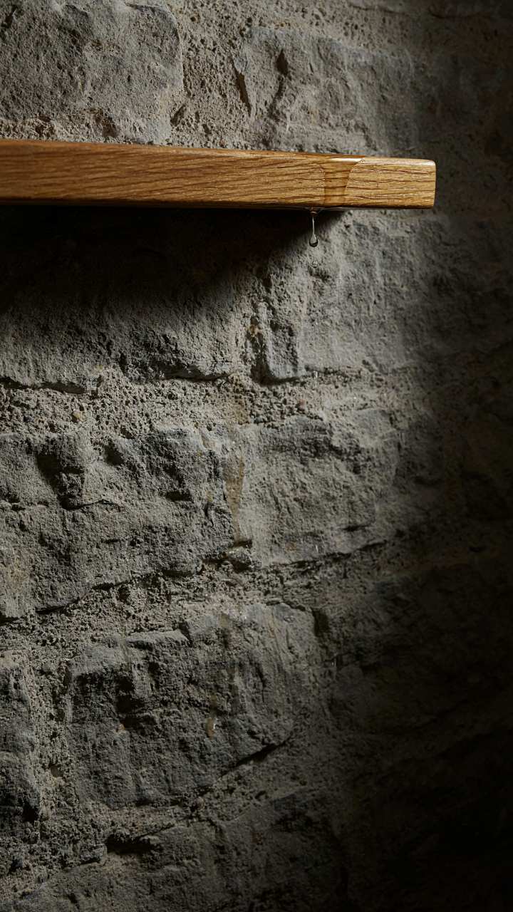Rough stone shower wall contrasts with a smooth wooden shelf.