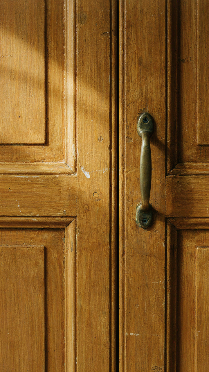 A close-up of a distressed ochre cabinet door with an antique handle.