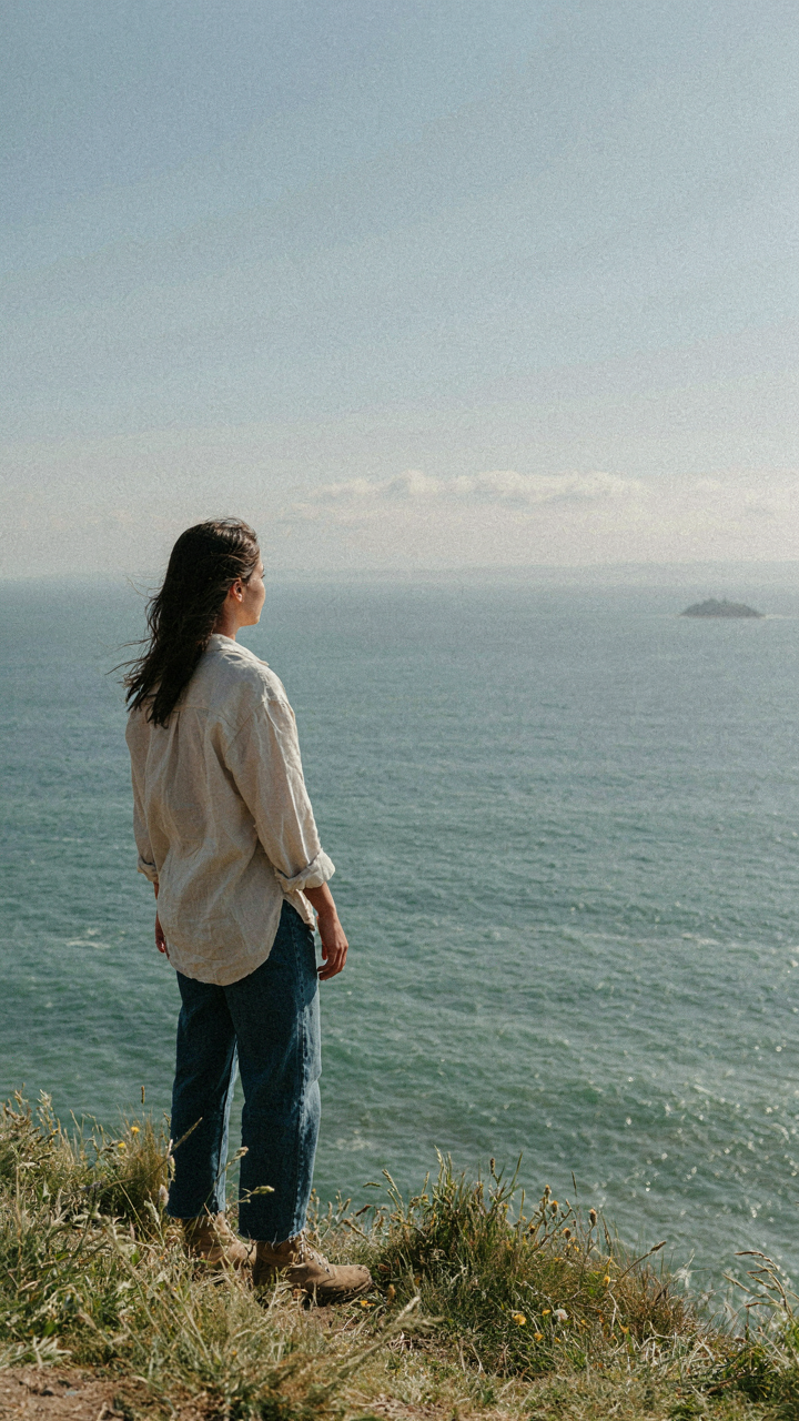 A person on a cliff looks at a tiny island far in the ocean.