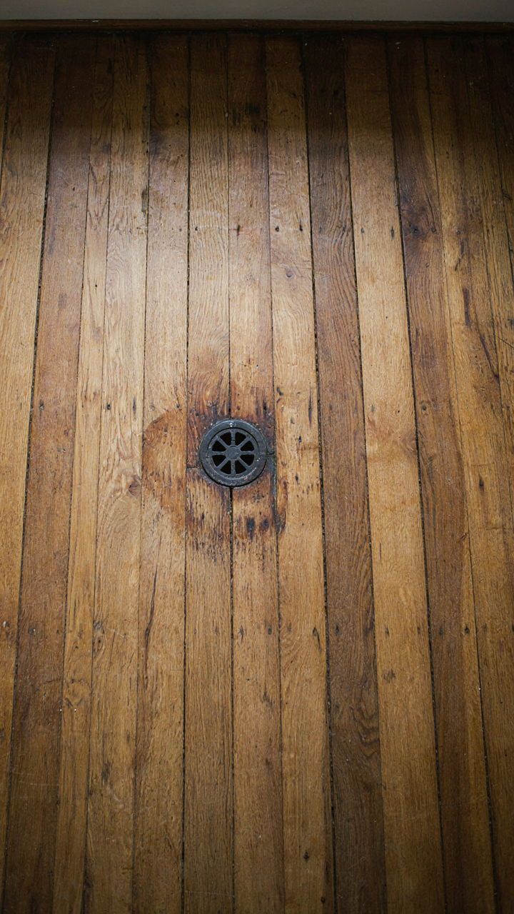 A reclaimed wide-plank wood floor with natural wear and a cast iron drain.