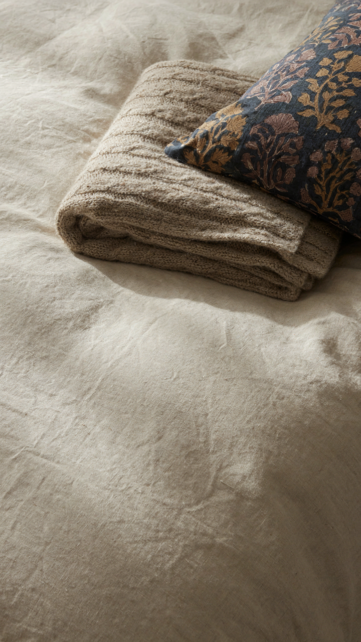 Close-up of a cream linen duvet with a wool blanket and silk pillow.
