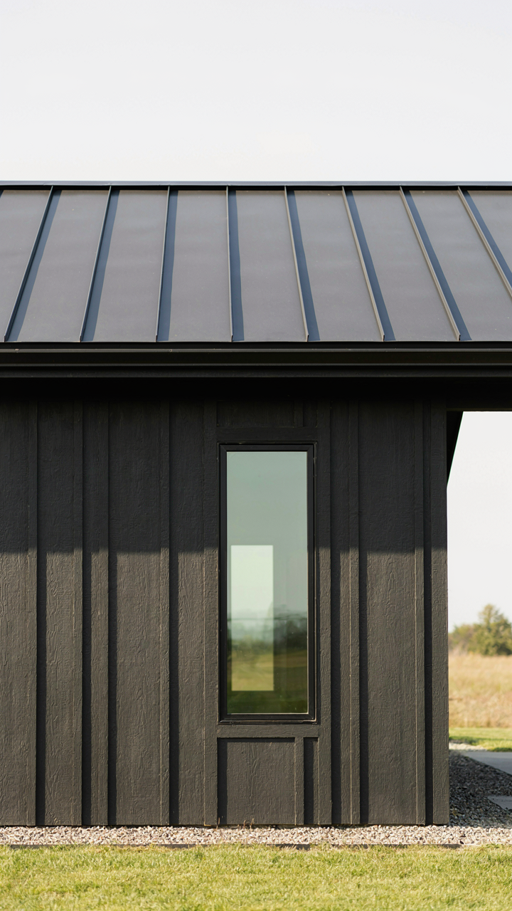 Modern ranch house exterior with dark fiber cement siding and a metal roof.
