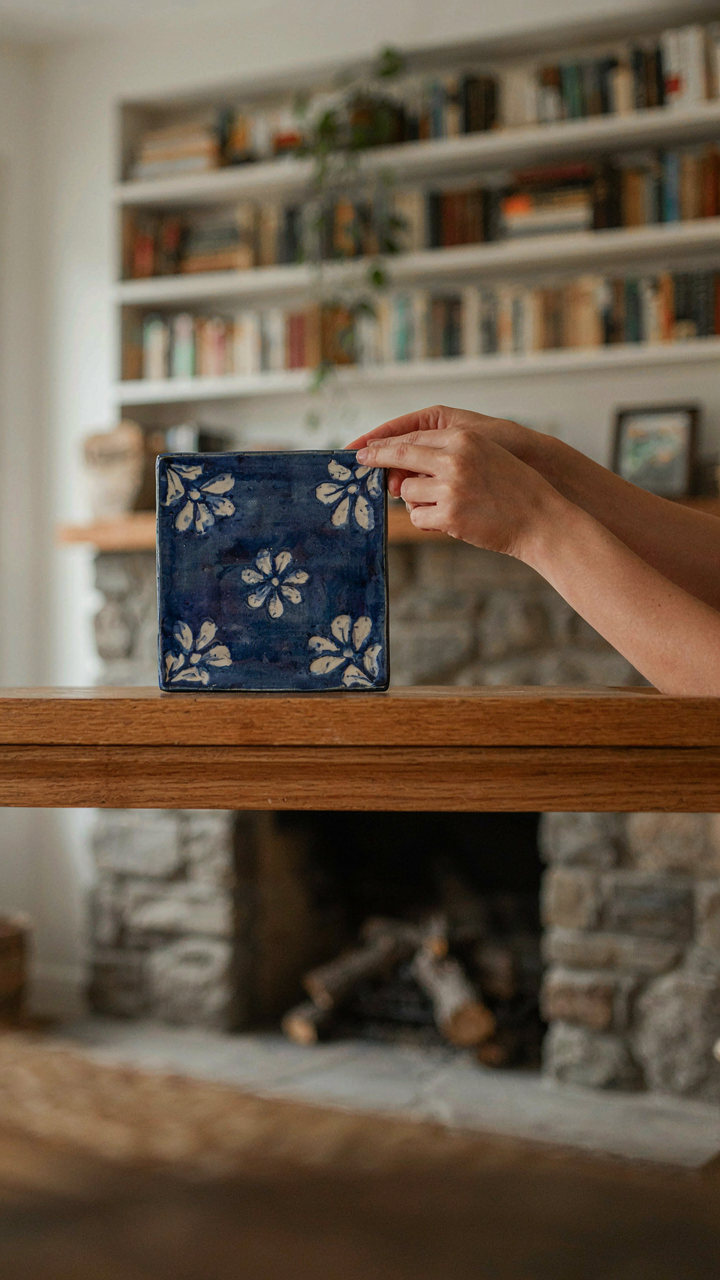 Hands placing a ceramic tile onto a craftsman fireplace mantel, surrounded by natural wood.