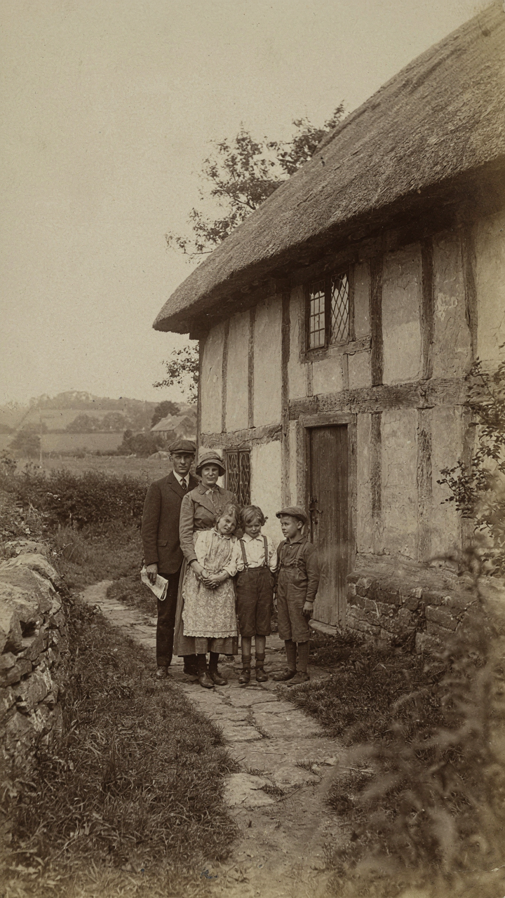 A vintage photo of a simple Tudor cottage with a family outside.