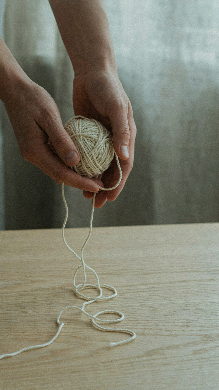 A person's hands letting go of a tangled ball of string.