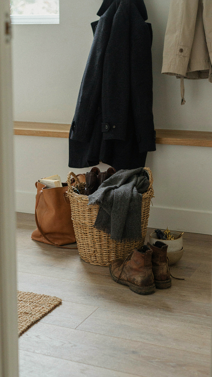 A simple wicker basket on the floor in a mudroom, collecting dropped items.