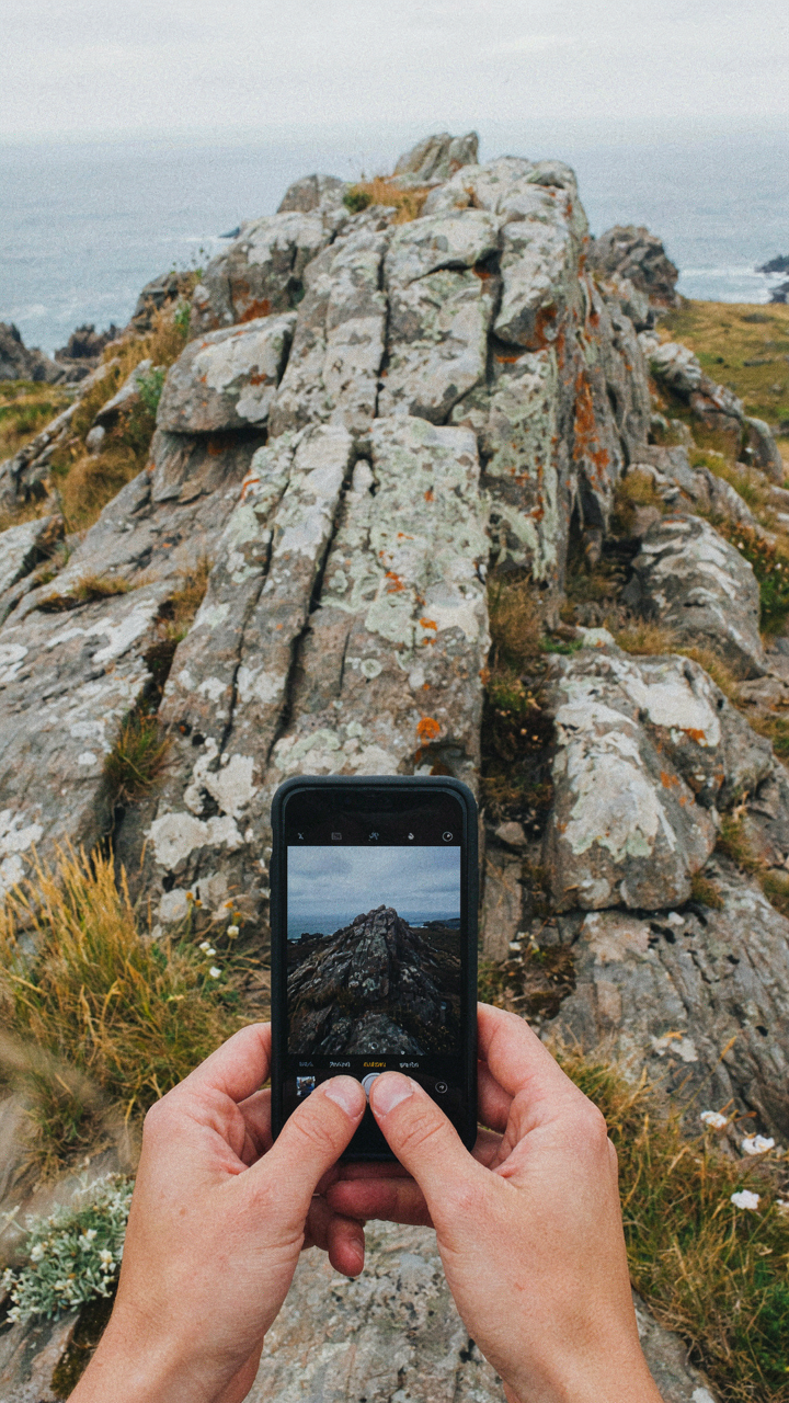 Hands hold a smartphone, taking a photo of a unique local stone outcropping.