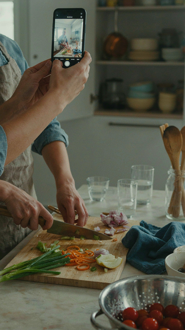 A person films themselves cooking in a kitchen on a smartphone.