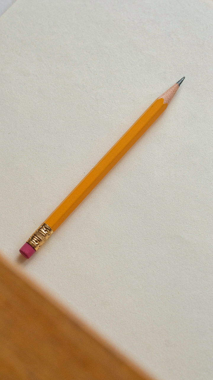 A sharpened pencil rests on a blank notebook page.
