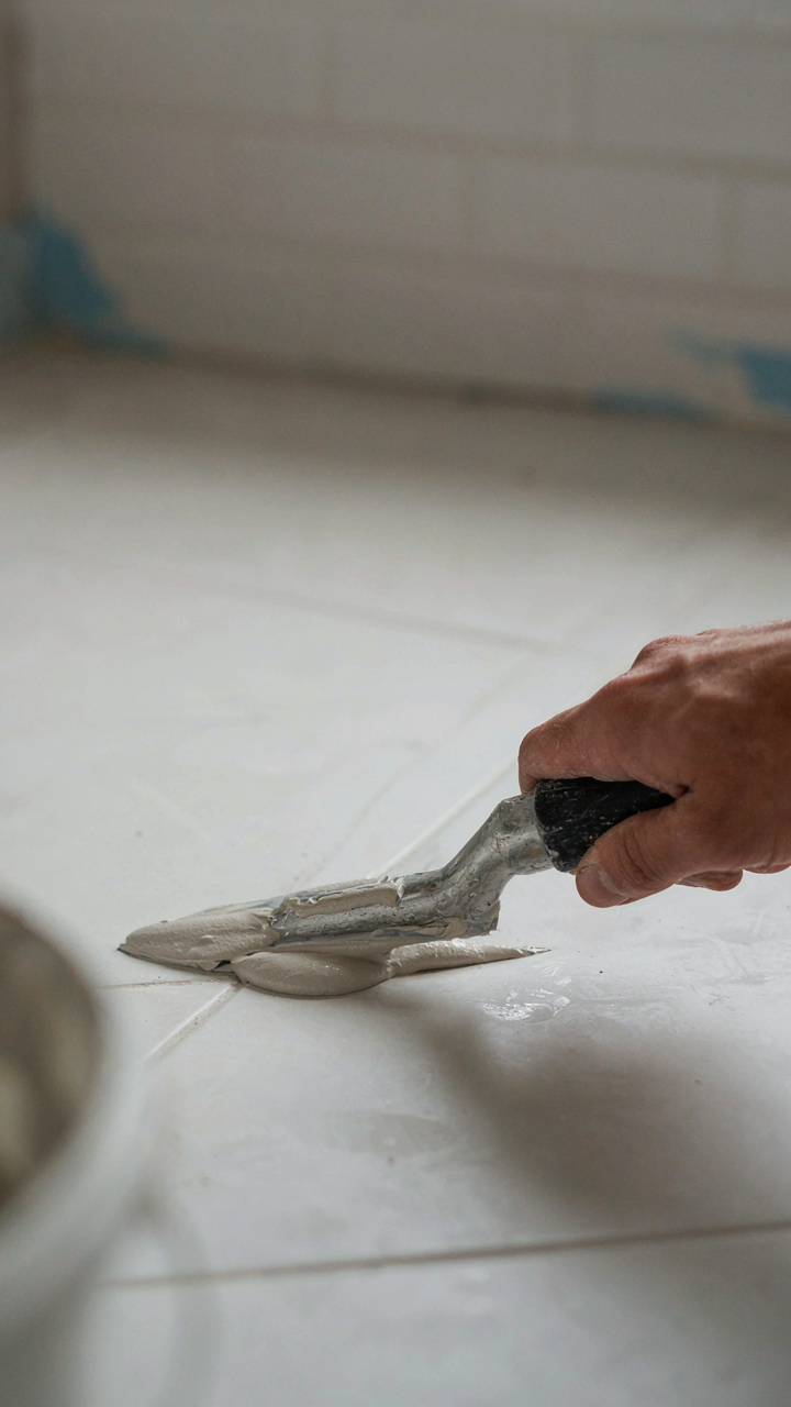 A hand applying epoxy grout between white subway tiles.