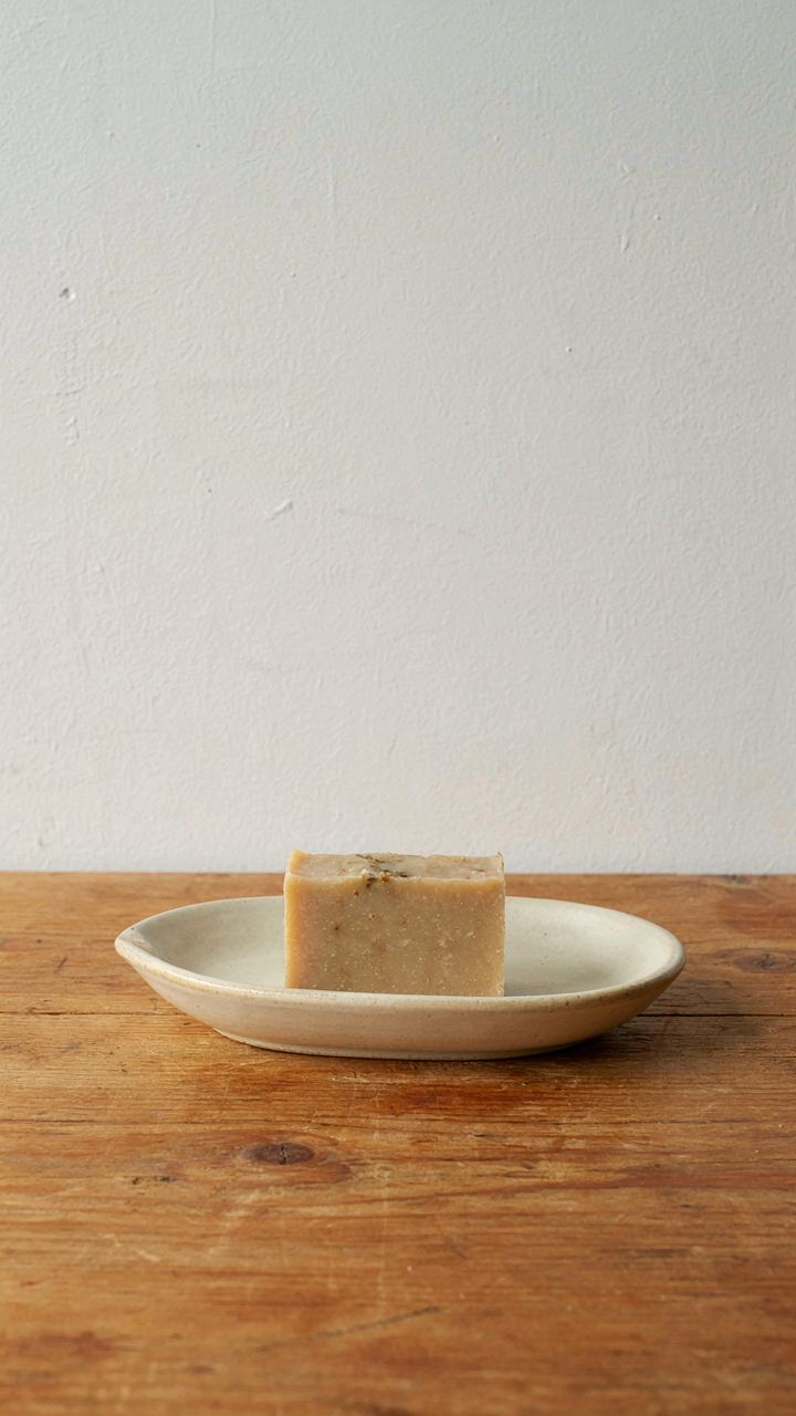 A single ceramic soap dish with a bar of soap on a clear wooden counter.