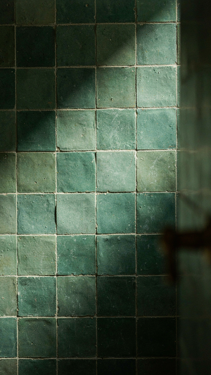 Green zellige tile shower wall shows uneven texture and light reflection.