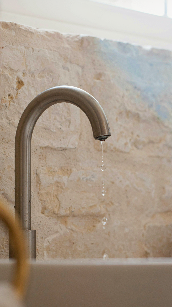 Matte stainless steel faucet and unsealed limestone showing patina in a coastal cottage bathroom.