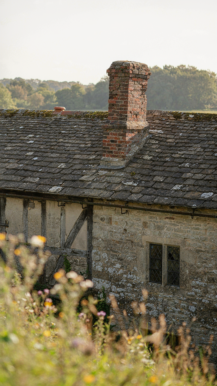 A crooked brick chimney on an old stone house with exposed timber framing.
