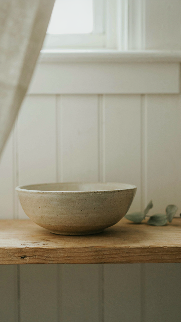 A single, hand-thrown ceramic bowl on a bare wooden shelf.