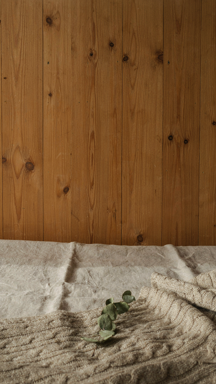 A close-up shows textures of raw wood, linen bedding, and a wool blanket.