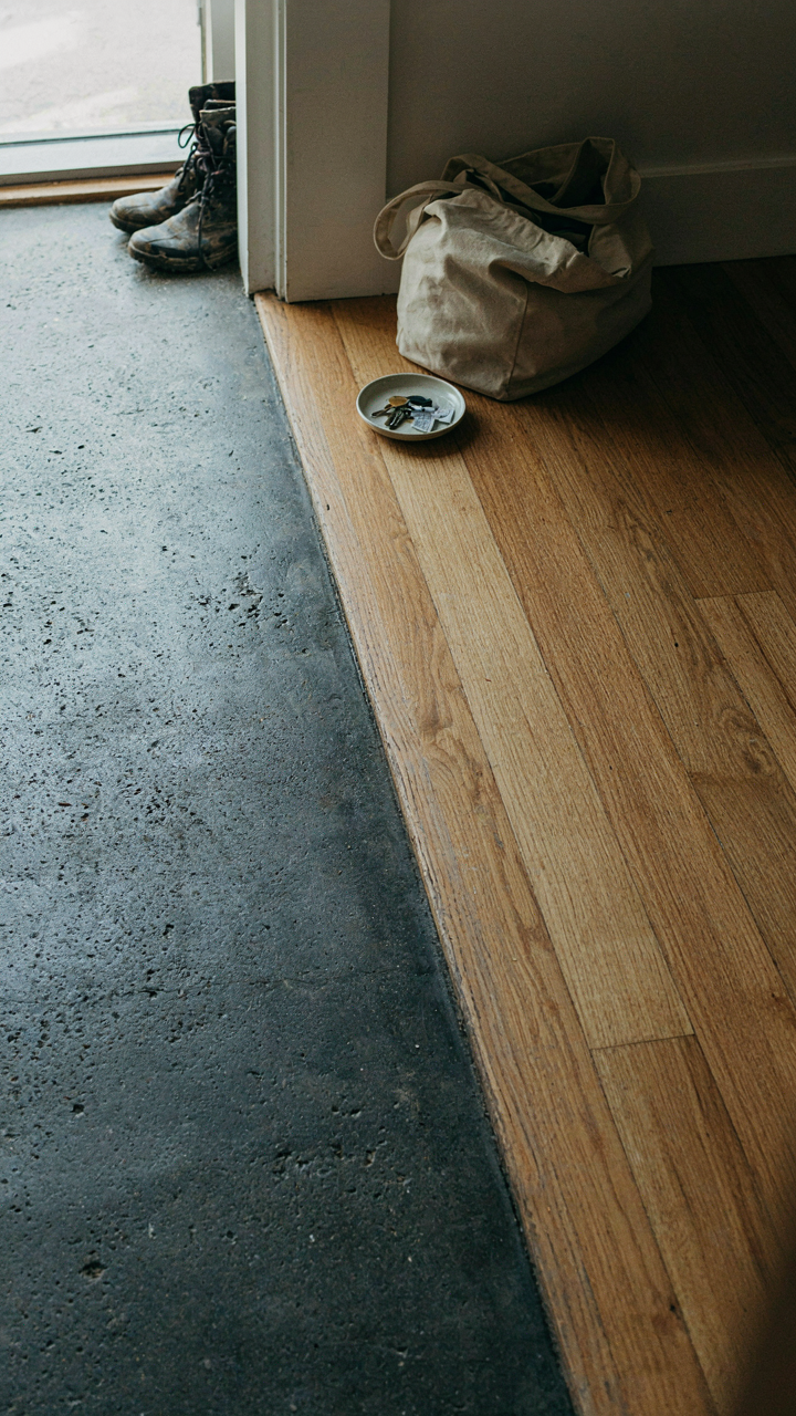 A clear boundary on the floor where concrete meets wood in a mudroom.