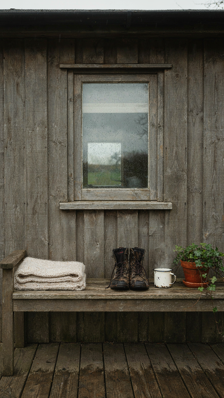 A deep porch on a tiny cottage with a bench and muddy boots.