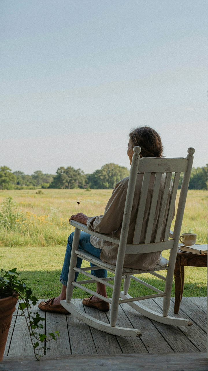 A person sits peacefully on a cottage porch chair, looking at the horizon.