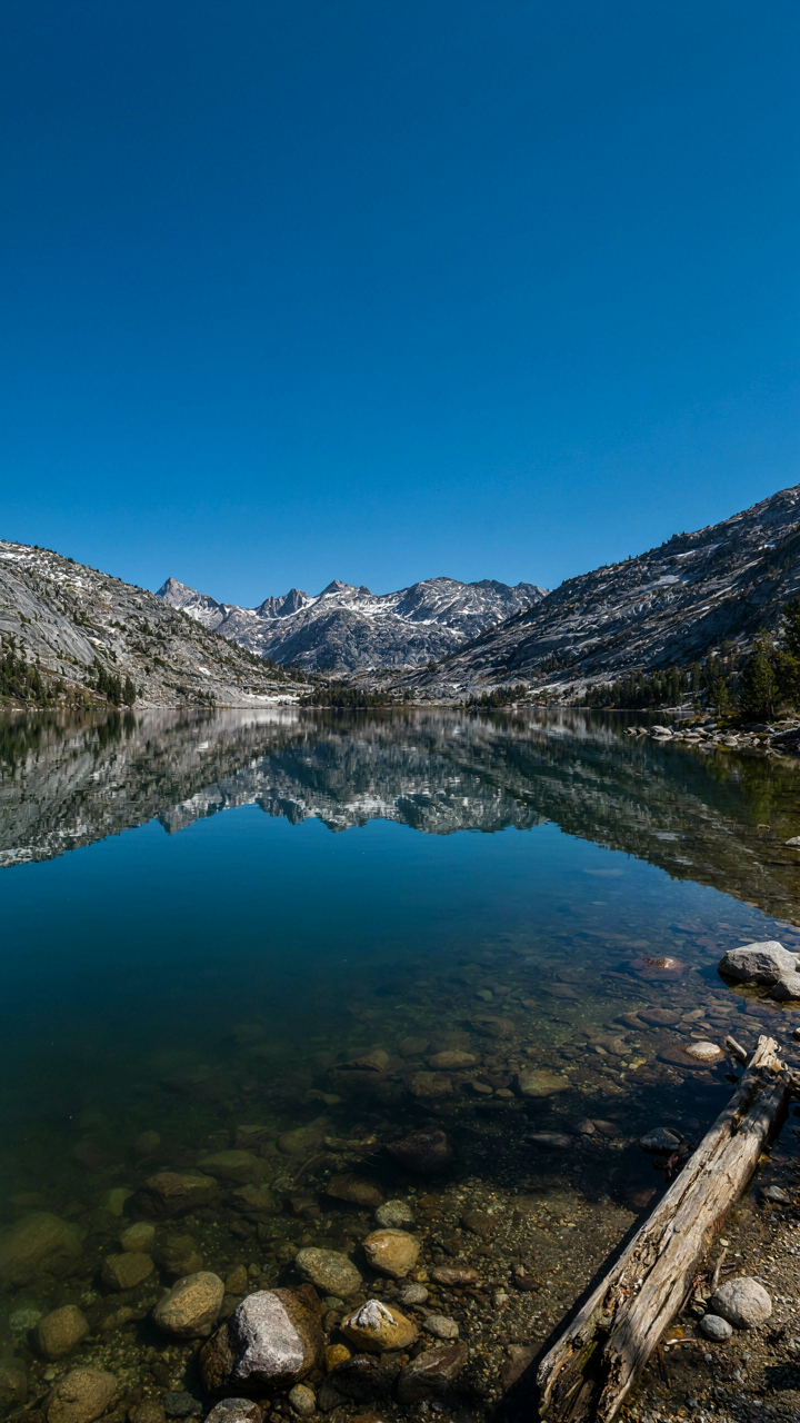 A clear, calm lake reflects a pristine blue sky and mountains.
