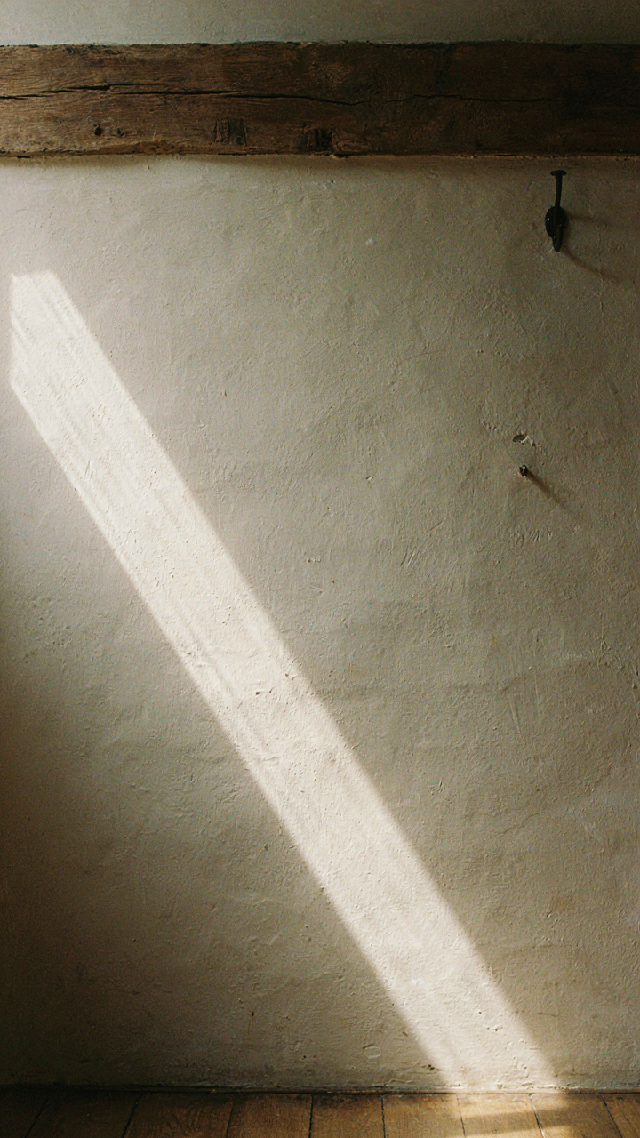 A beam of sunlight highlights dark oak and textured plaster in a Tudor room.
