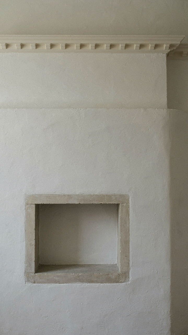 Dentil cornice above a simple fireplace, casting shadows in a Georgian room.
