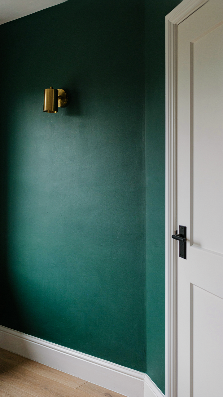 A bedroom with an emerald green feature wall and white trim.