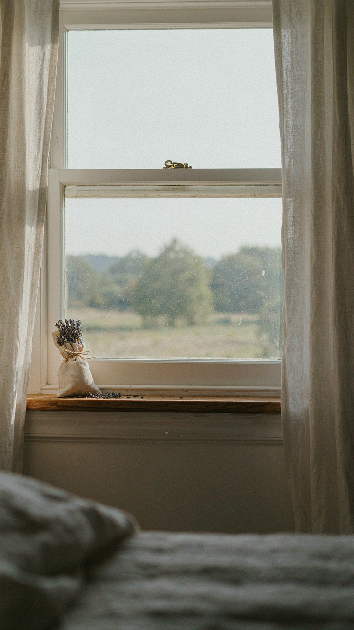 An open window in a farmhouse bedroom brings in natural light and scent.