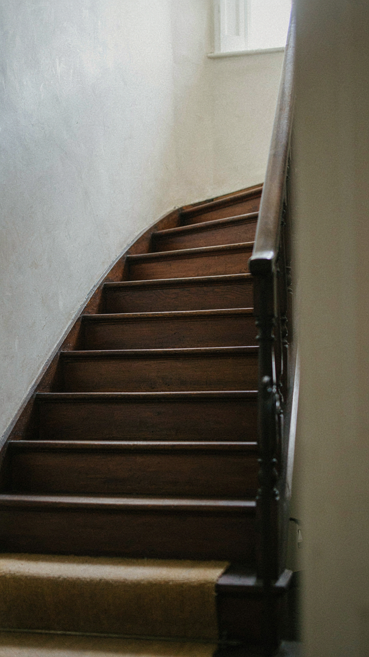 A narrow, steep cottage staircase with dark wood and a simple handrail.