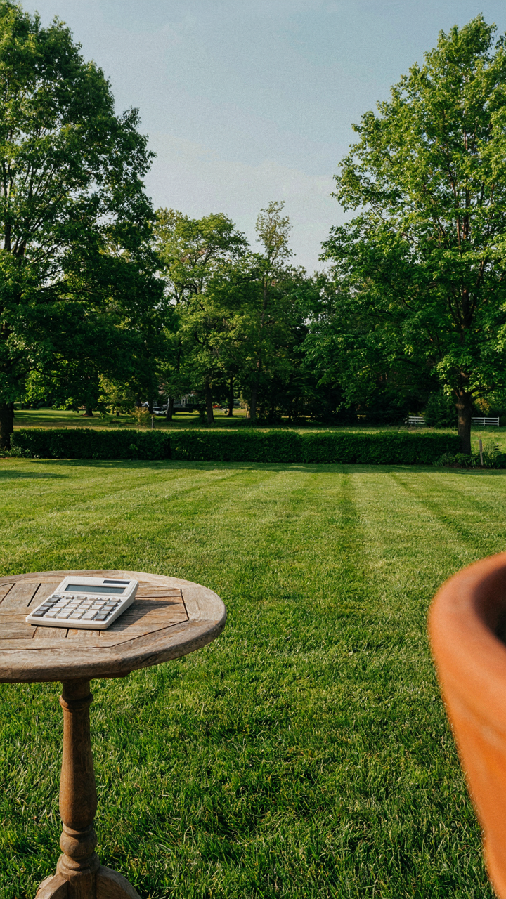 A calculator on a table in an empty, manicured backyard.