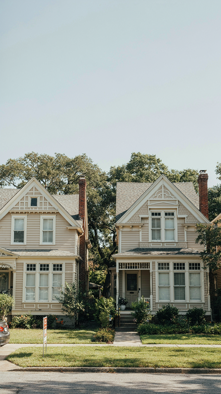 Two nearly identical beige Victorian houses, one with a 'For Sale' sign.