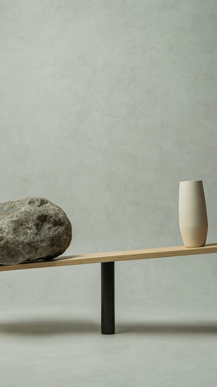 A seesaw with a large boulder on one side and a vase on the other.