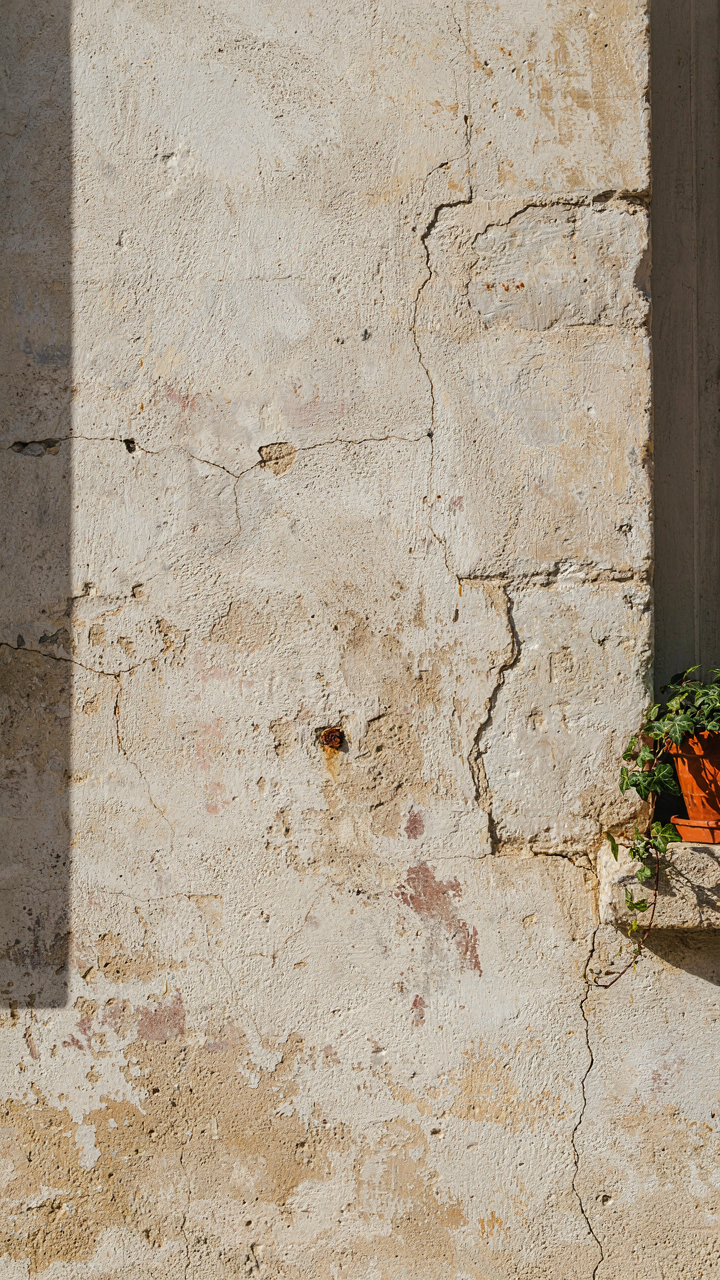 A close-up of a French cottage wall with cracks and uneven whitewash.