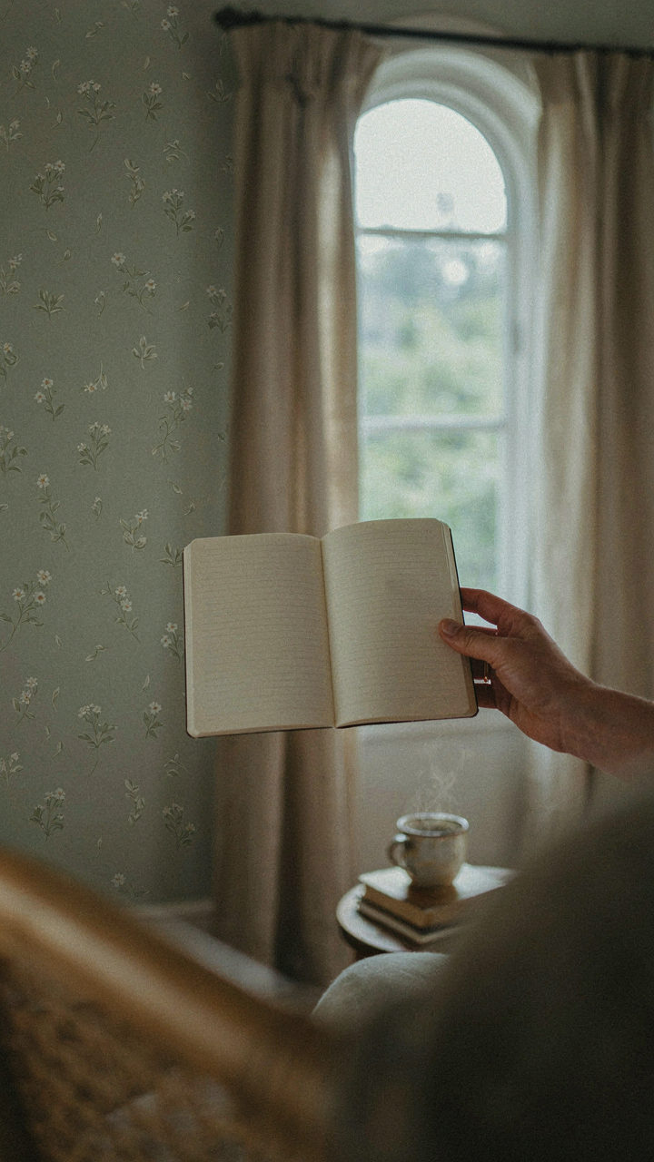 A hand holds a notebook with three words, looking at an intentional room.