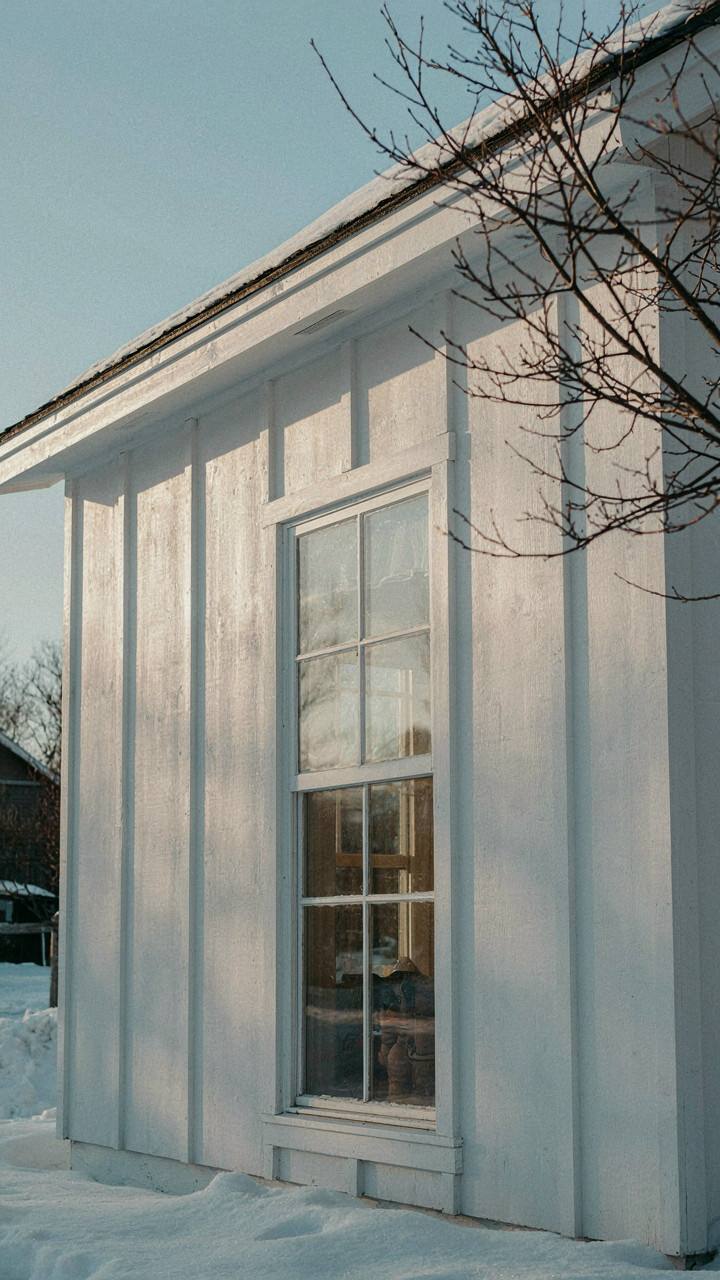 Sunlight reflects brightly off a white cottage exterior wall and into a window.